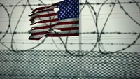 Tattered American flag seen through barbed wire
