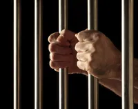 Picture of hands grasping at prison bars on a black background