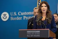 Kristi Noem addresses the nation behind a podium bearing a Nazi slogan