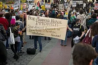 protesters carrying a sign that says, 'Free Mahmoud Khalil Immediately! Stop fascist assault on basic rights + academic freedom @theRevComs.'