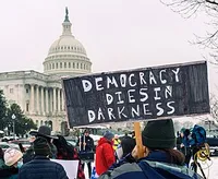 Protestors holding up a sign reading 'Democracy dies in darkness.'